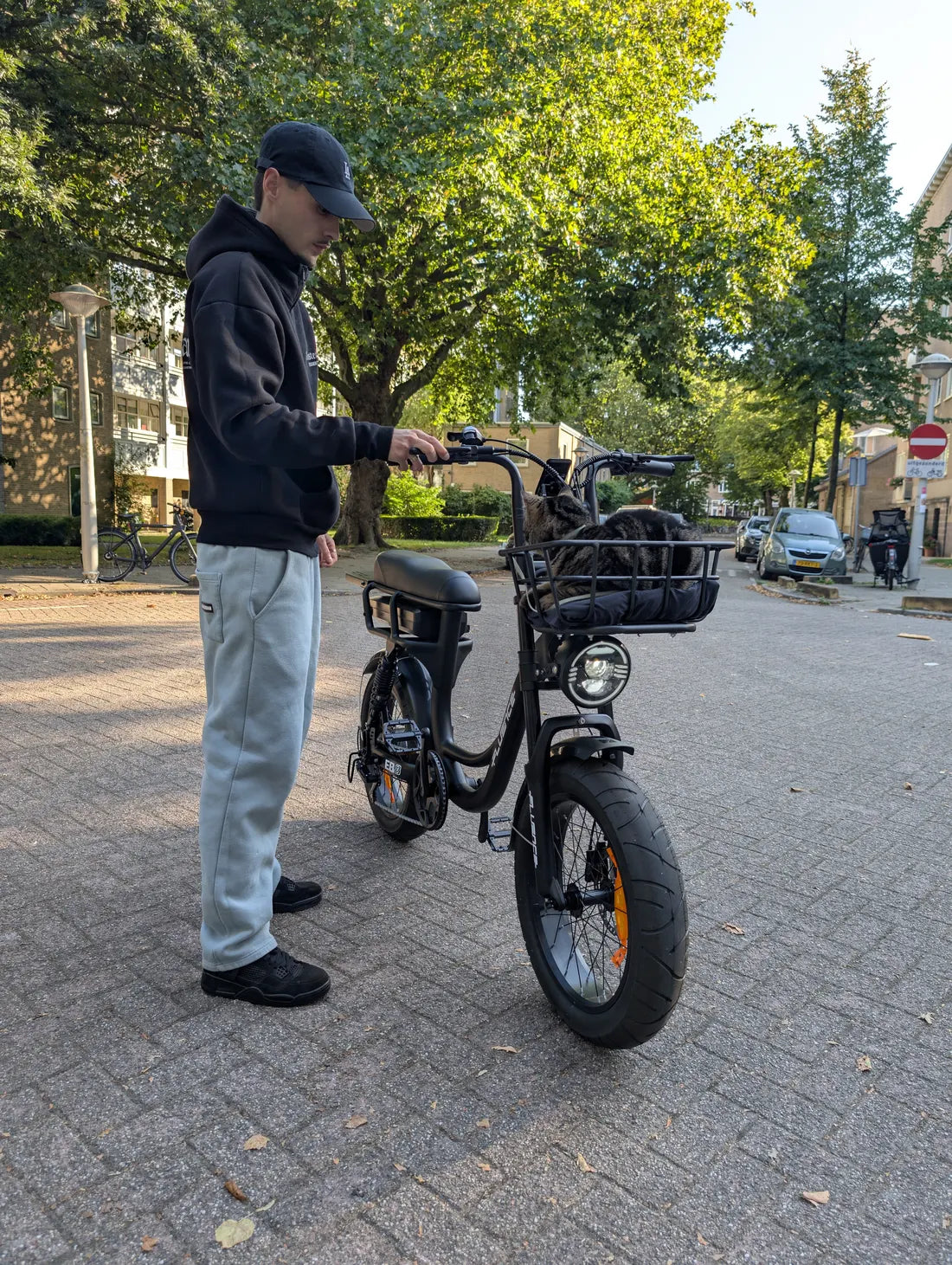 Un homme debout à côté du vélo électrique noir, dans une rue arborée